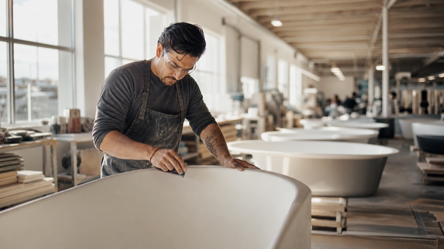 An American Bath Group craftsperson finishing a freestanding bathtub in a US manufacturing facility